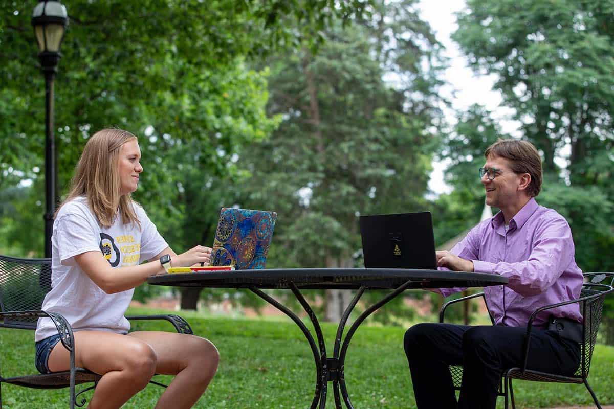 Professor Peter Sheldon meets with a student at an outdoor table.
